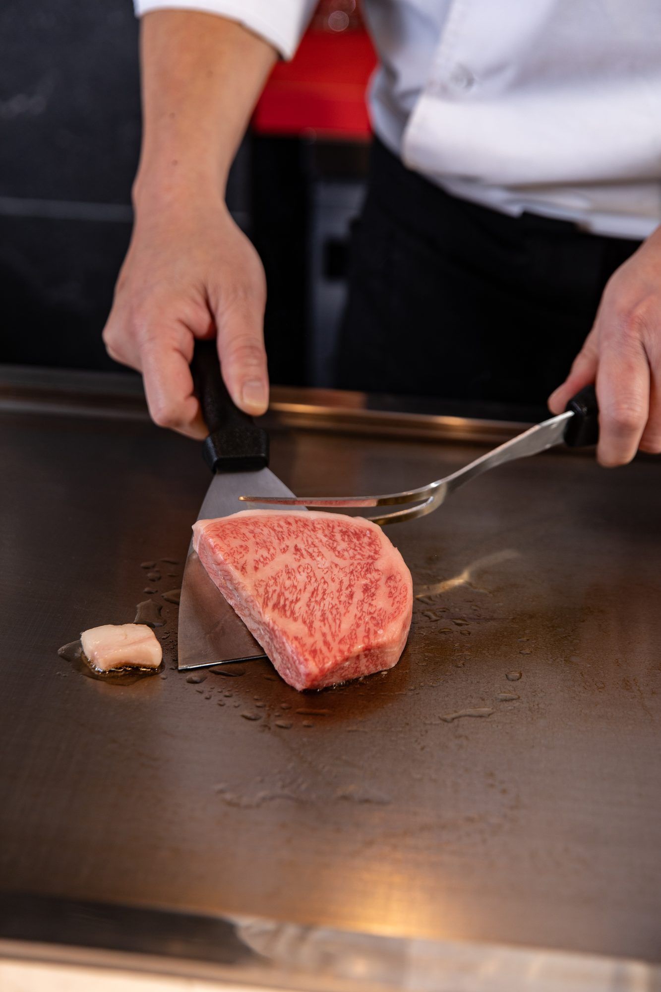 Hands placing Kobe beef on the iron plate with spatula and fork as grilling begins